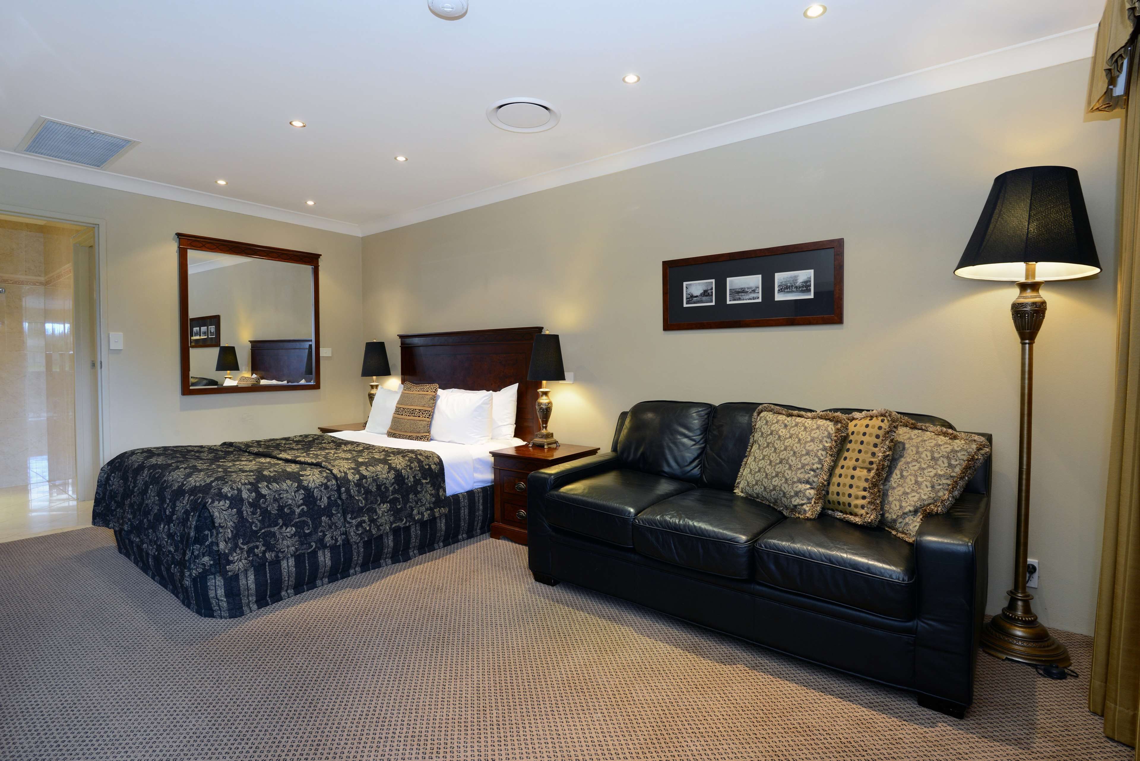 A hotel room with a bed, a black leather sofa, a nightstand, a lamp, and a framed picture on the wall.