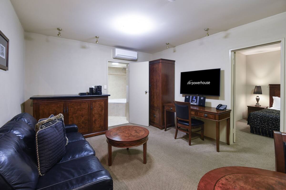 A living room with a leather sofa, a wooden coffee table, a TV, a desk with a chair, and a wardrobe.