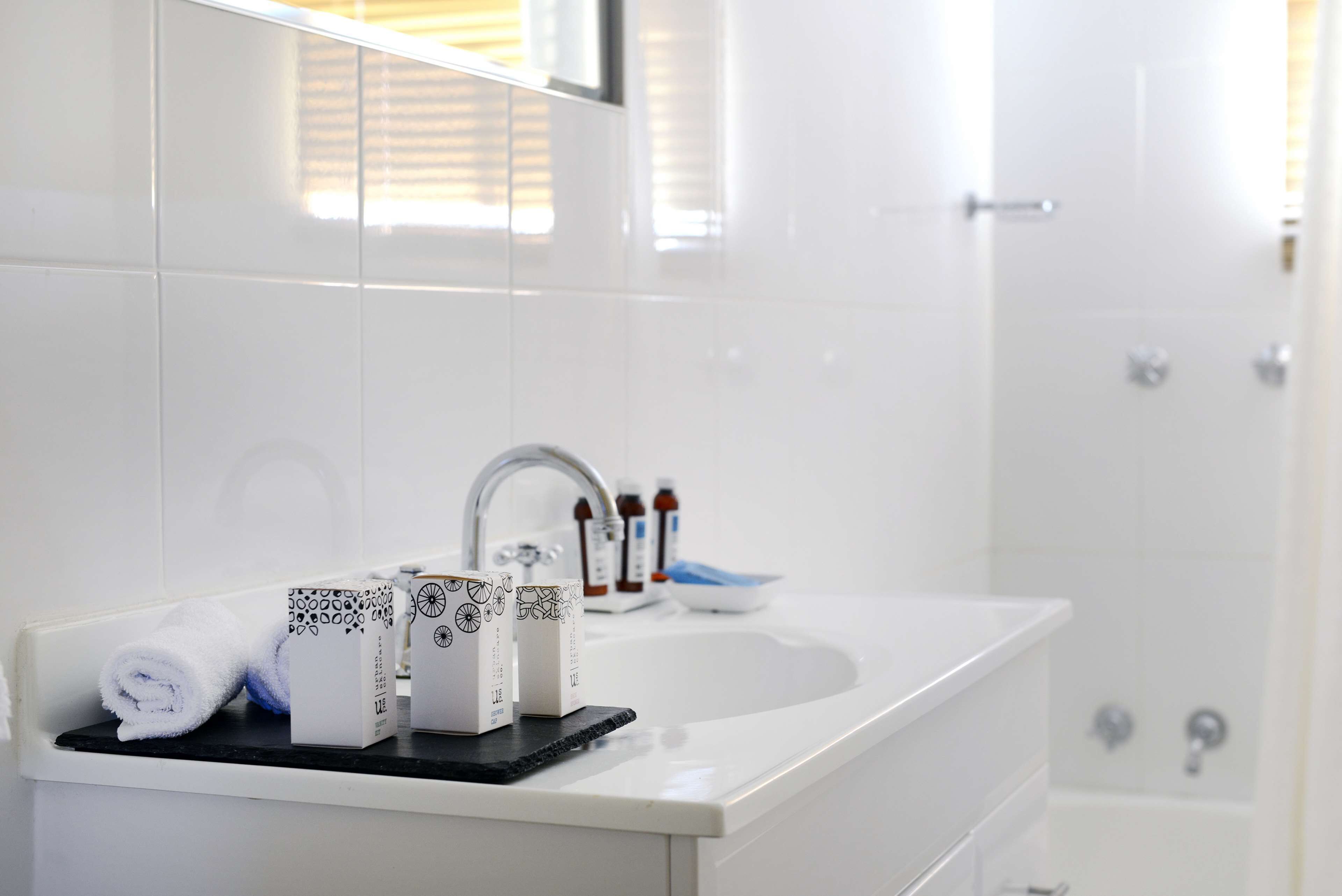 Een badkamer met een witte wastafel, een spiegel en een handdoekrek met opgerolde handdoeken.