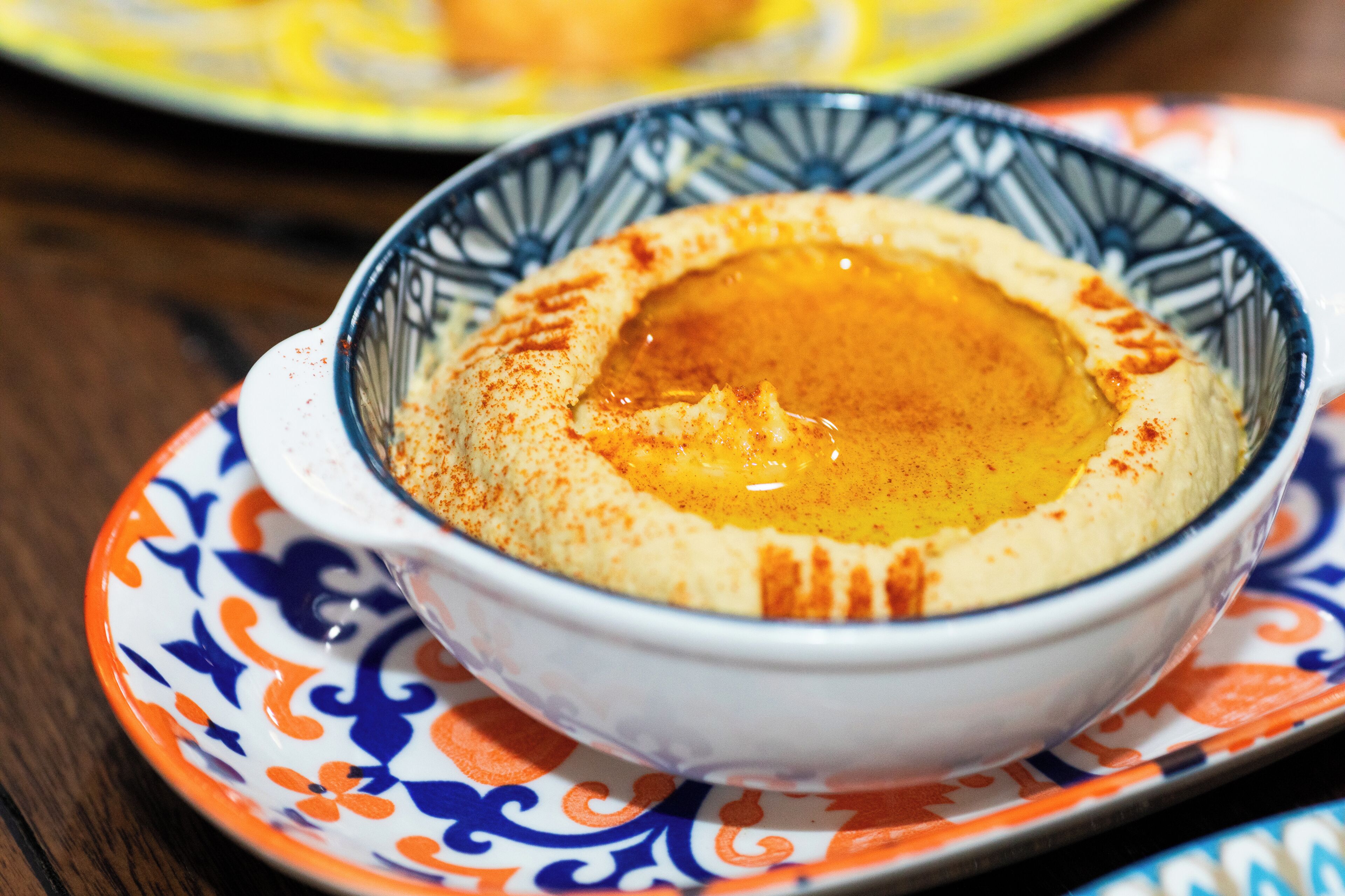 A bowl of hummus with a decorative rim on a patterned plate.