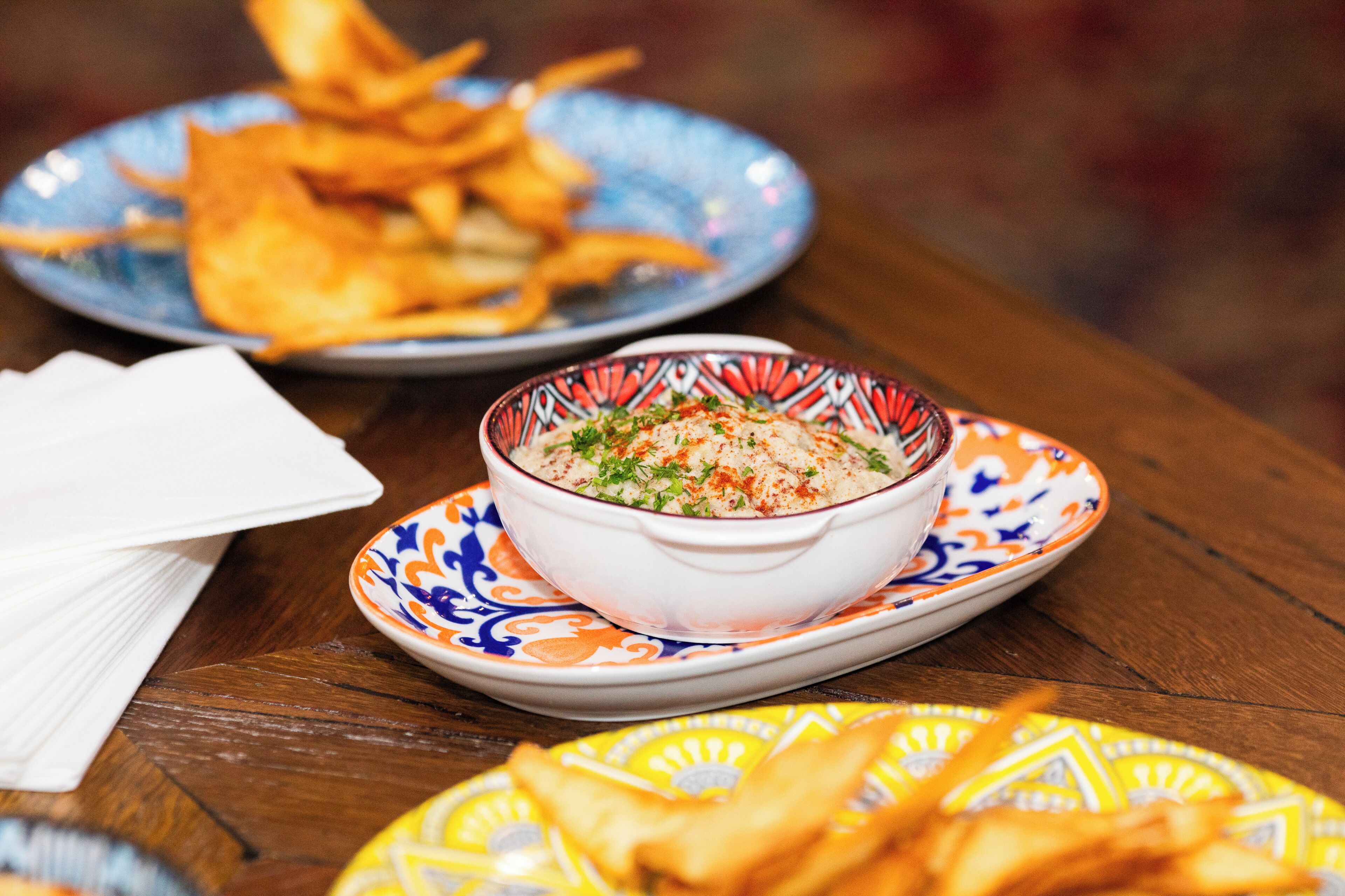 A table with a bowl of food, plates of fries, and a napkin.