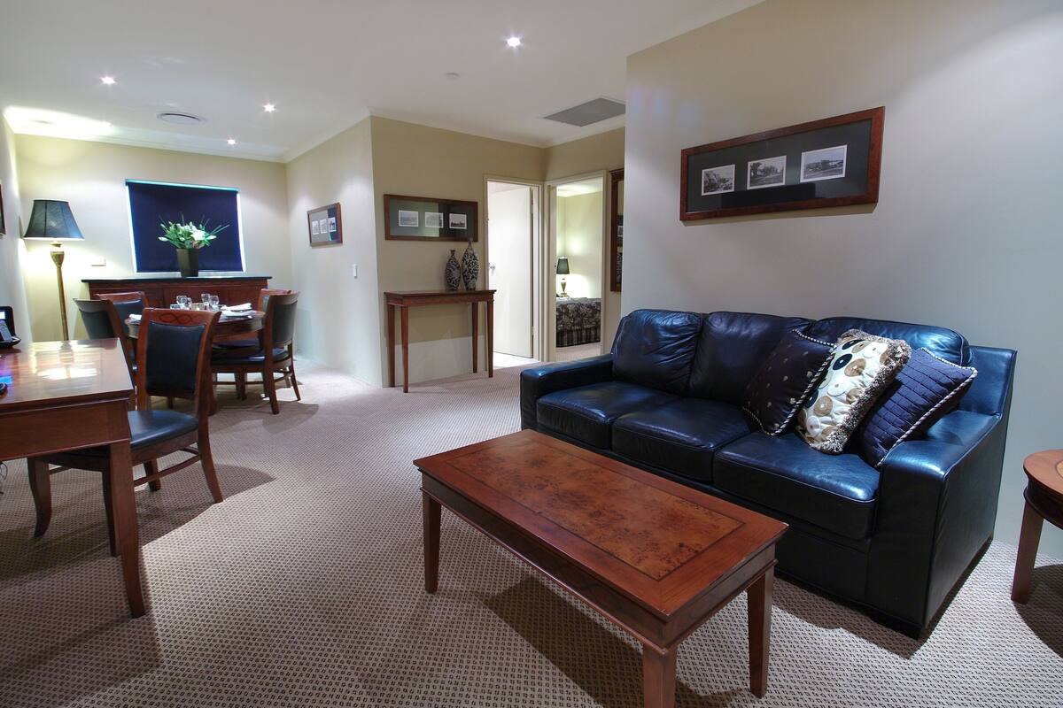A living room with a blue leather sofa, a wooden coffee table, and a dining area with a table and chairs.