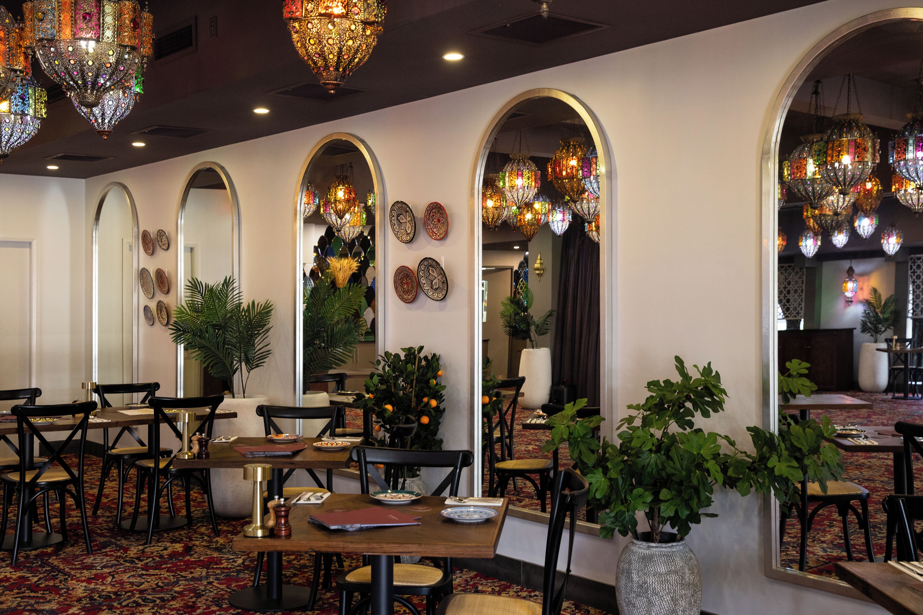 A restaurant interior with multiple dining tables, chairs, and hanging decorative lights.