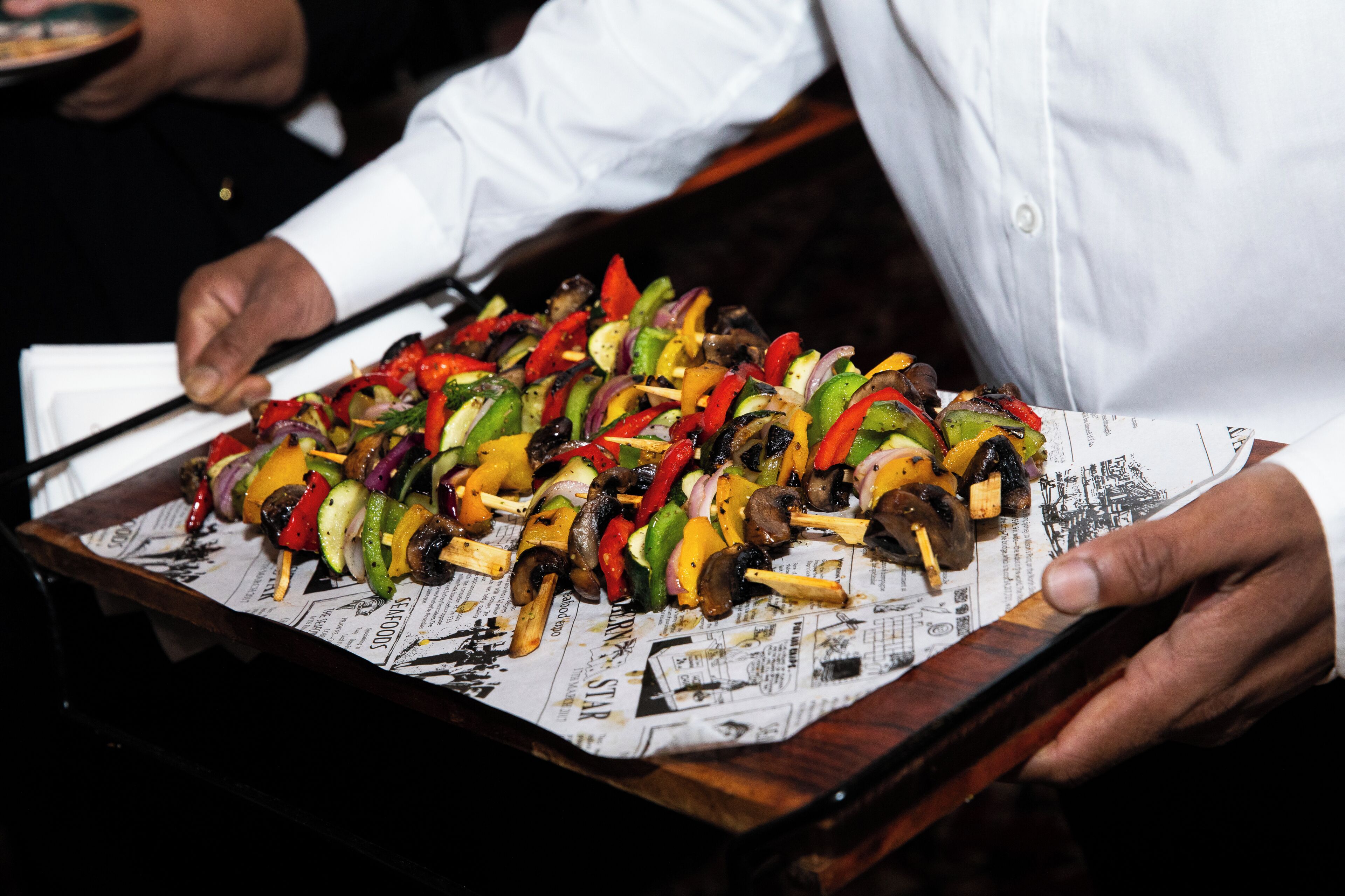 A tray of vegetable skewers on a newspaper-lined tray.