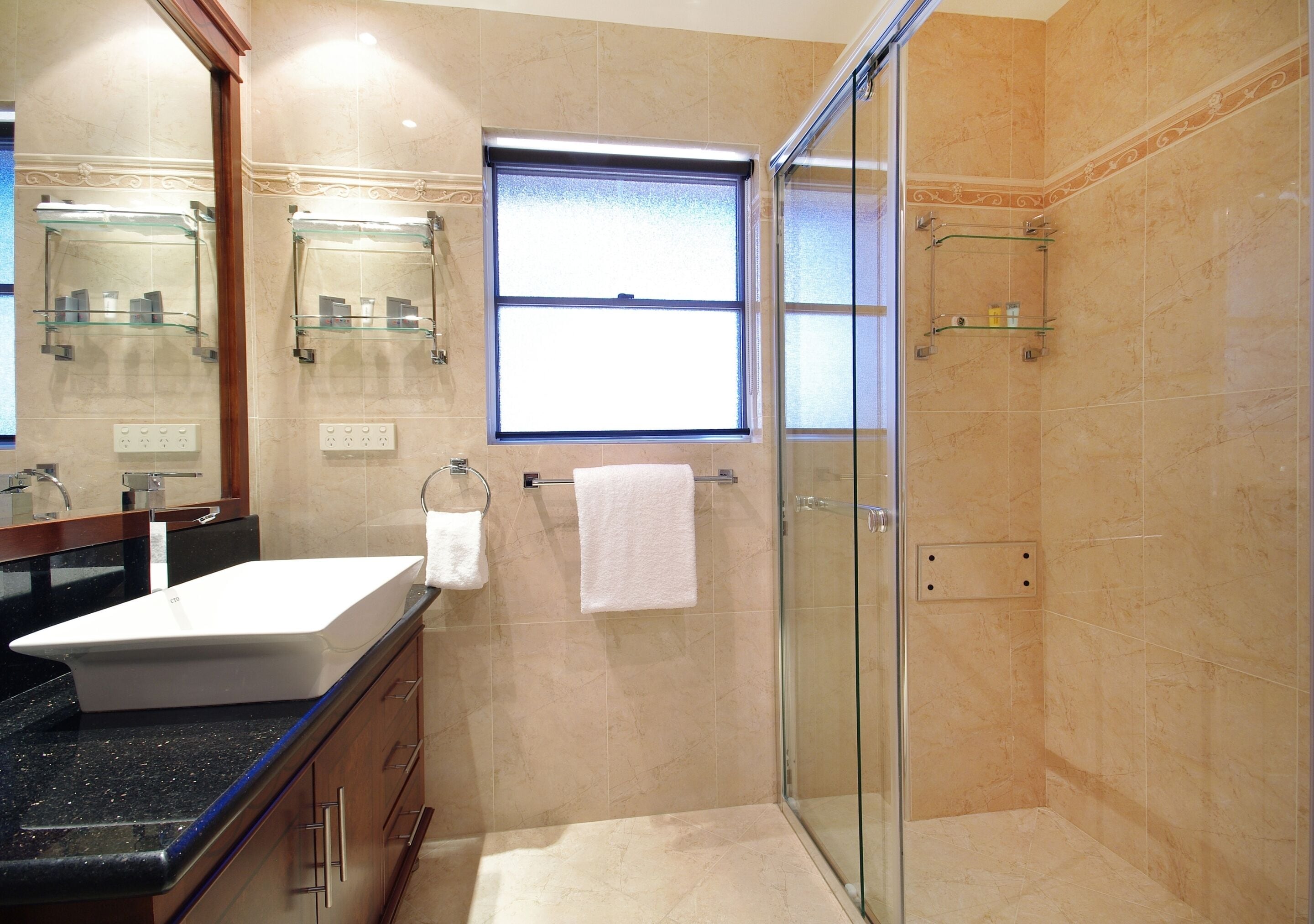 A modern bathroom with a large sink, glass shower enclosure, and a window providing natural light.