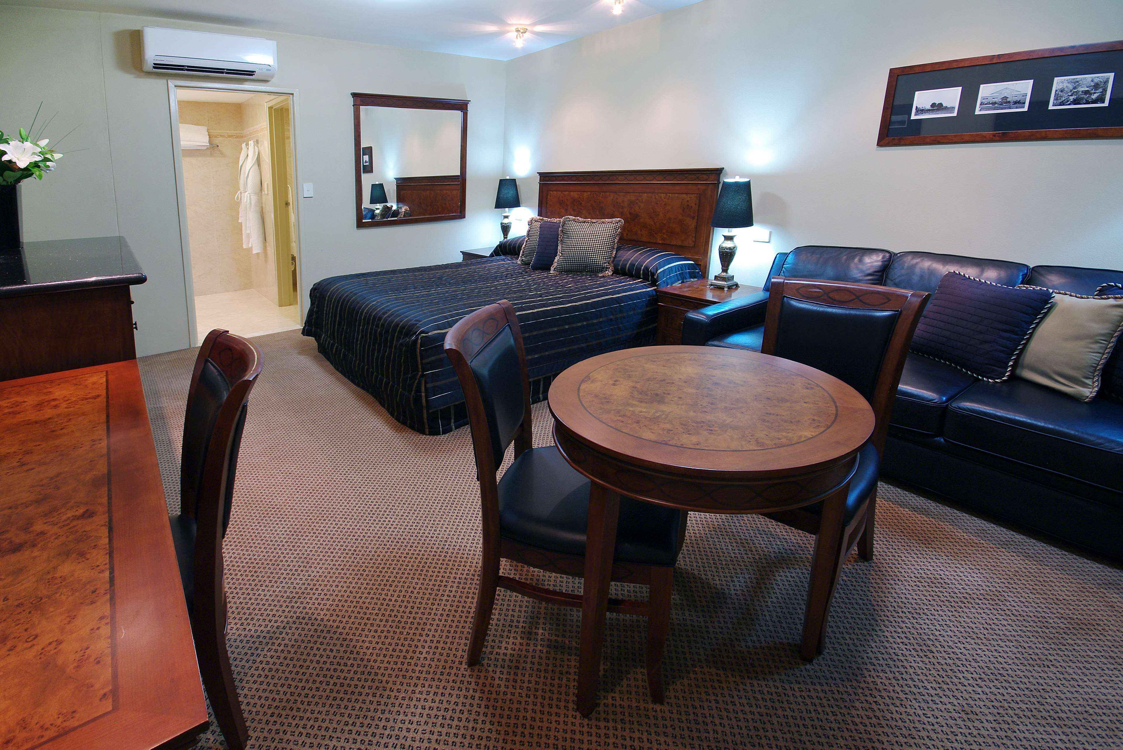 A hotel room with a bed, a sofa, a dining table, and a chair. There is a mirror on the wall and a picture frame above the sofa.