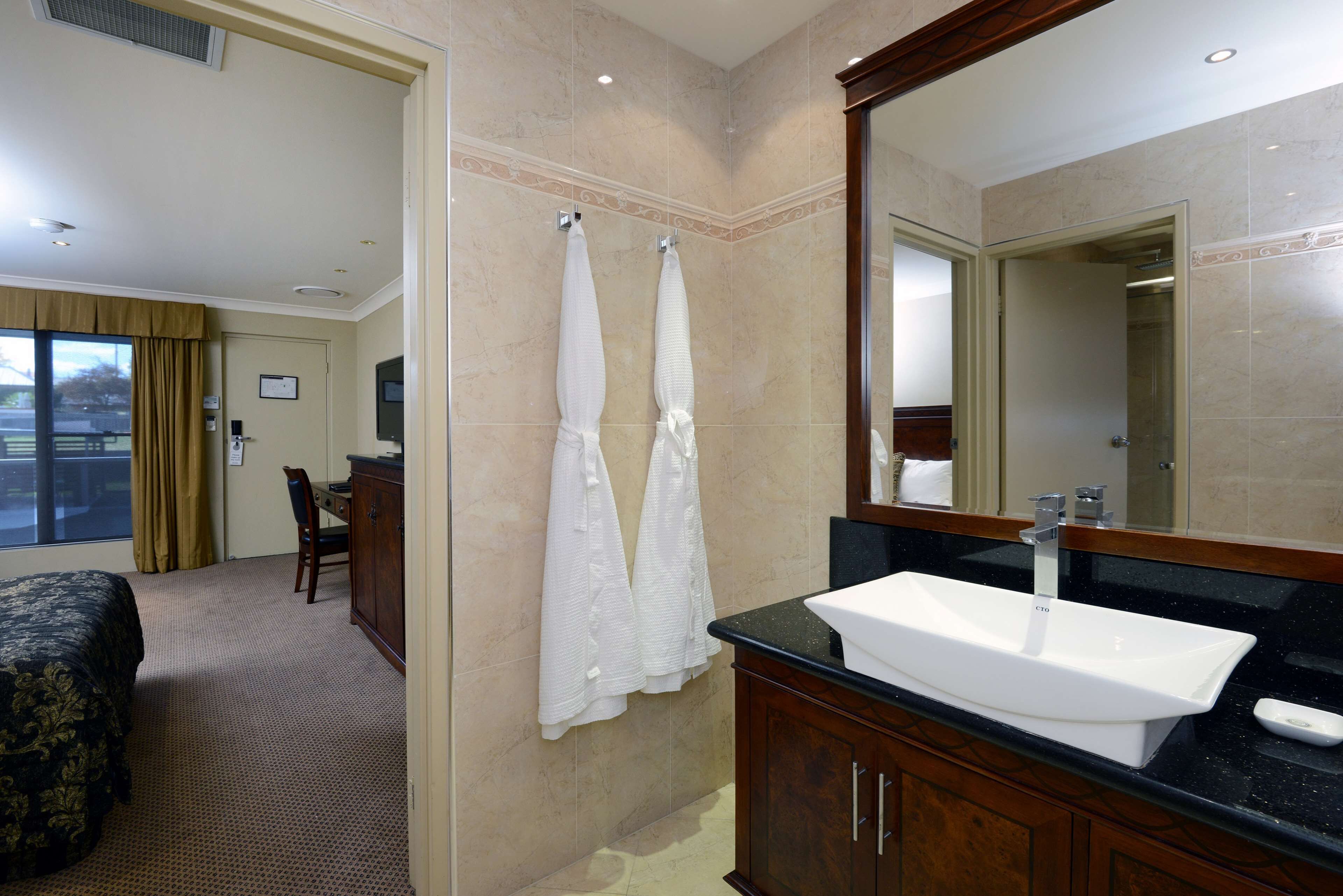 Une salle de bain d’hôtel avec un grand lavabo, un miroir et deux serviettes accrochées au mur.