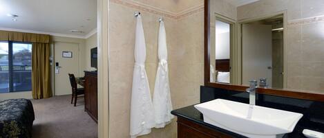 Une salle de bain d’hôtel avec un grand lavabo, un miroir et deux serviettes accrochées au mur.