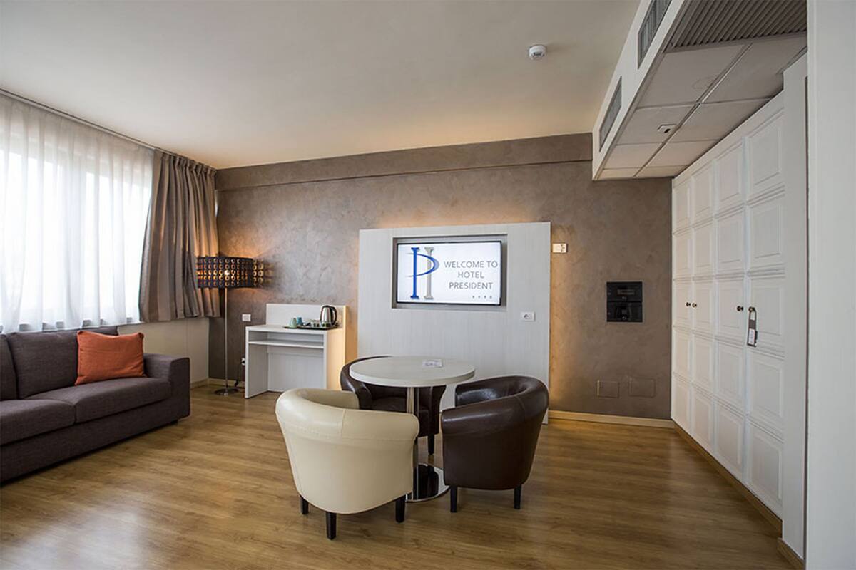 Una habitación de hotel moderna con sofá, dos sillones, una mesita, escritorio y armario.