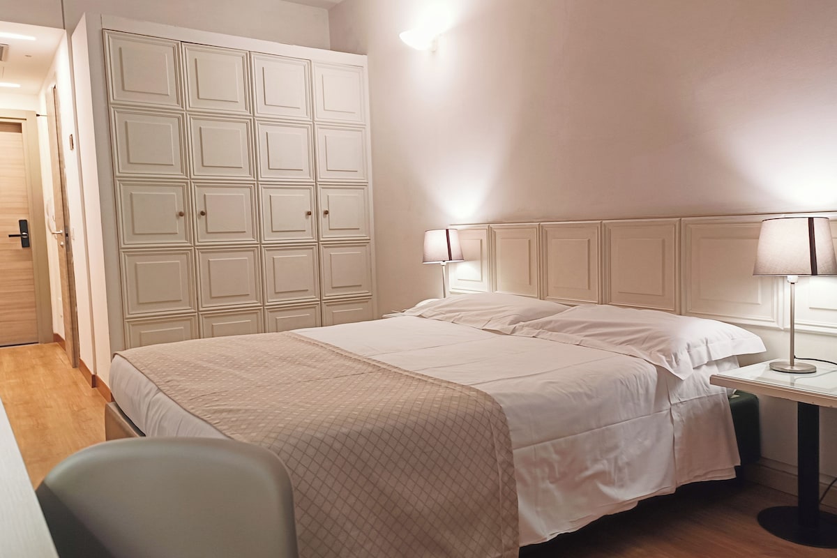 A neatly arranged bedroom with a bed, bedside lamps, a wardrobe, and a desk.