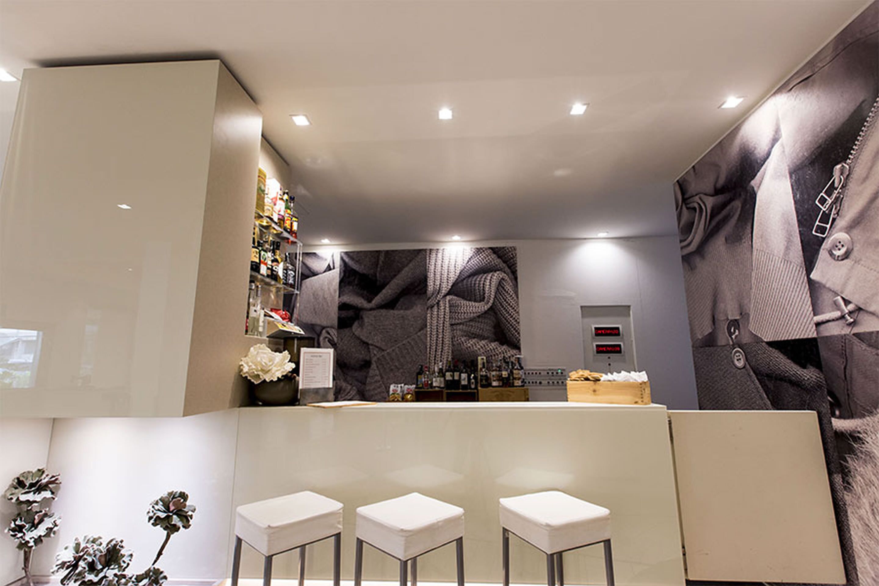 A modern bar area with a counter, three white stools, and a wall with a large abstract pattern.