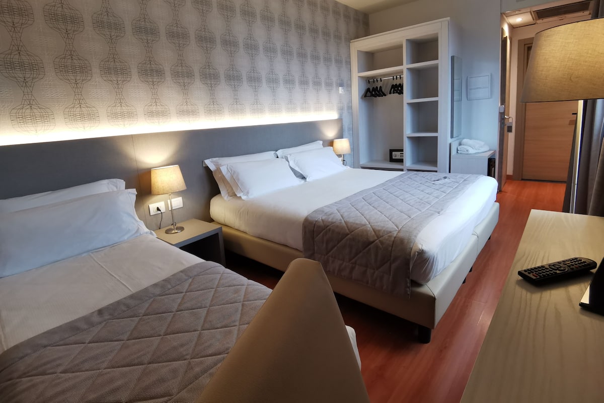 Una habitación de hotel con dos camas, un armario, un escritorio con lámpara y un televisor.
