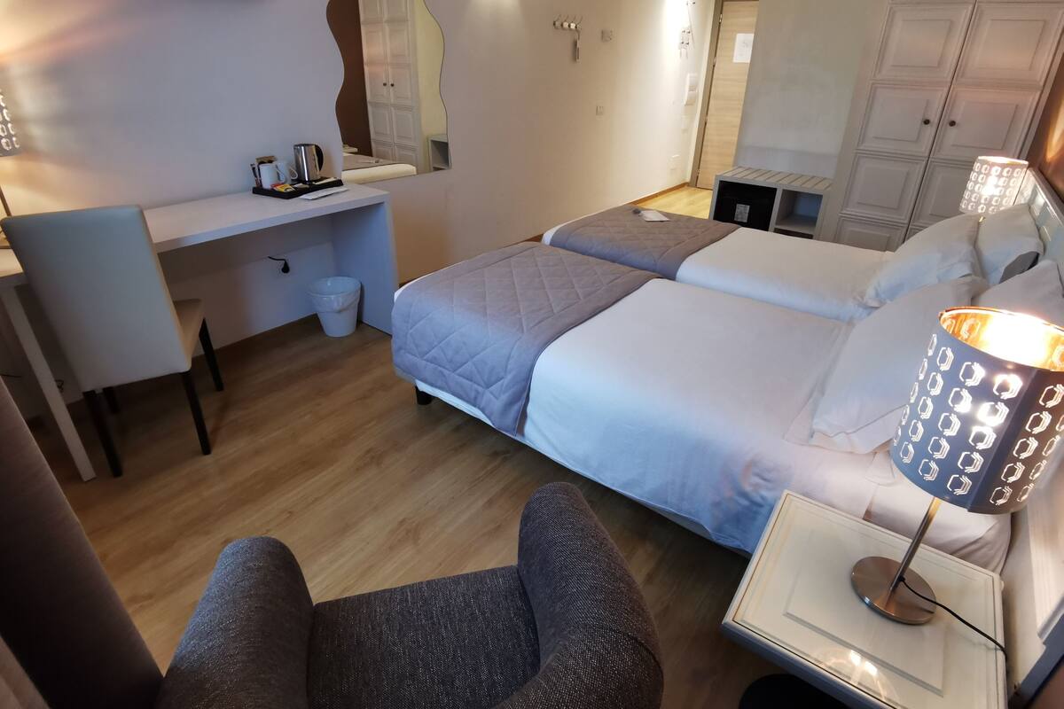 Una habitación de hotel con cama, escritorio, silla, lámpara y armario.