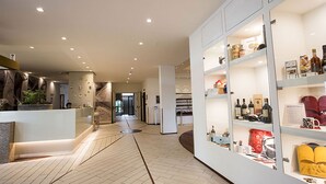 Un interior moderno con una mesa de recepción, una escalera y estanterías con diversos objetos.