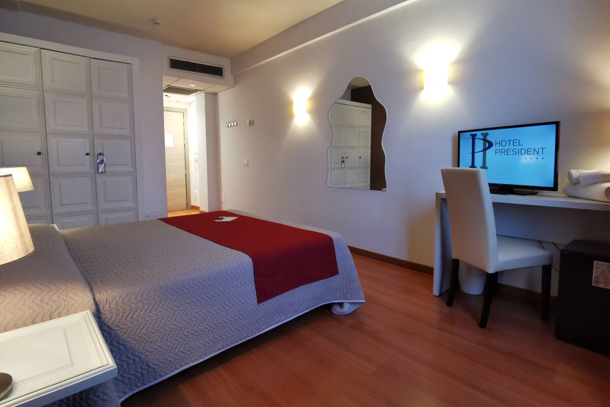 Habitación de hotel con cama, escritorio, silla, televisor y armario.