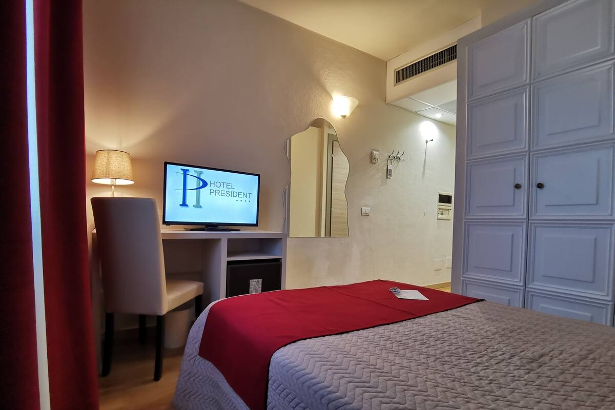Una habitación de hotel con una cama, un escritorio con computadora, un espejo y un armario.