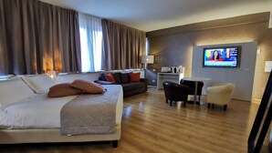 Habitación de hotel con cama, sofá, escritorio, silla y televisor en la pared.