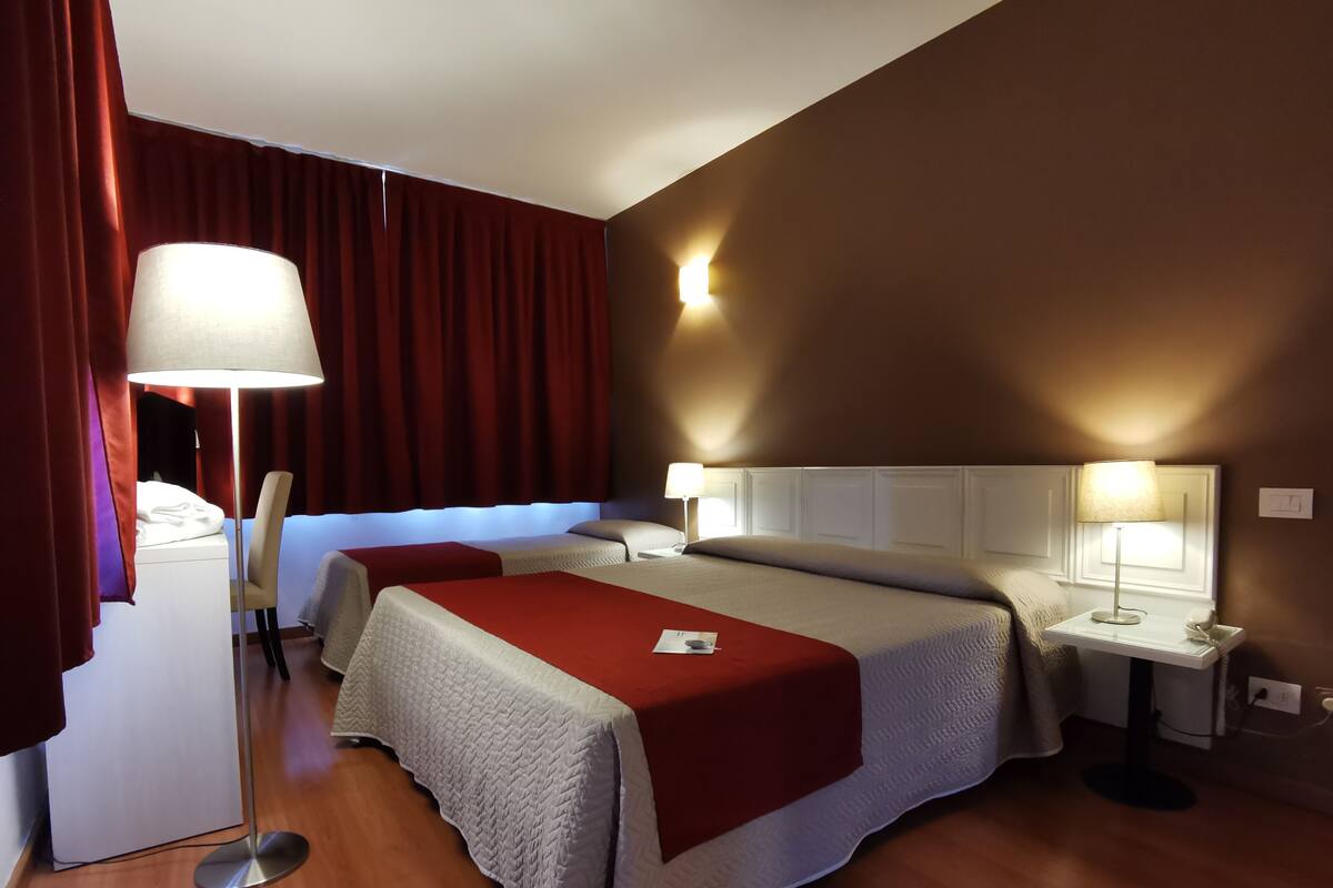 Habitación de hotel con dos camas, un escritorio, una silla y una mesita de noche con lámpara.