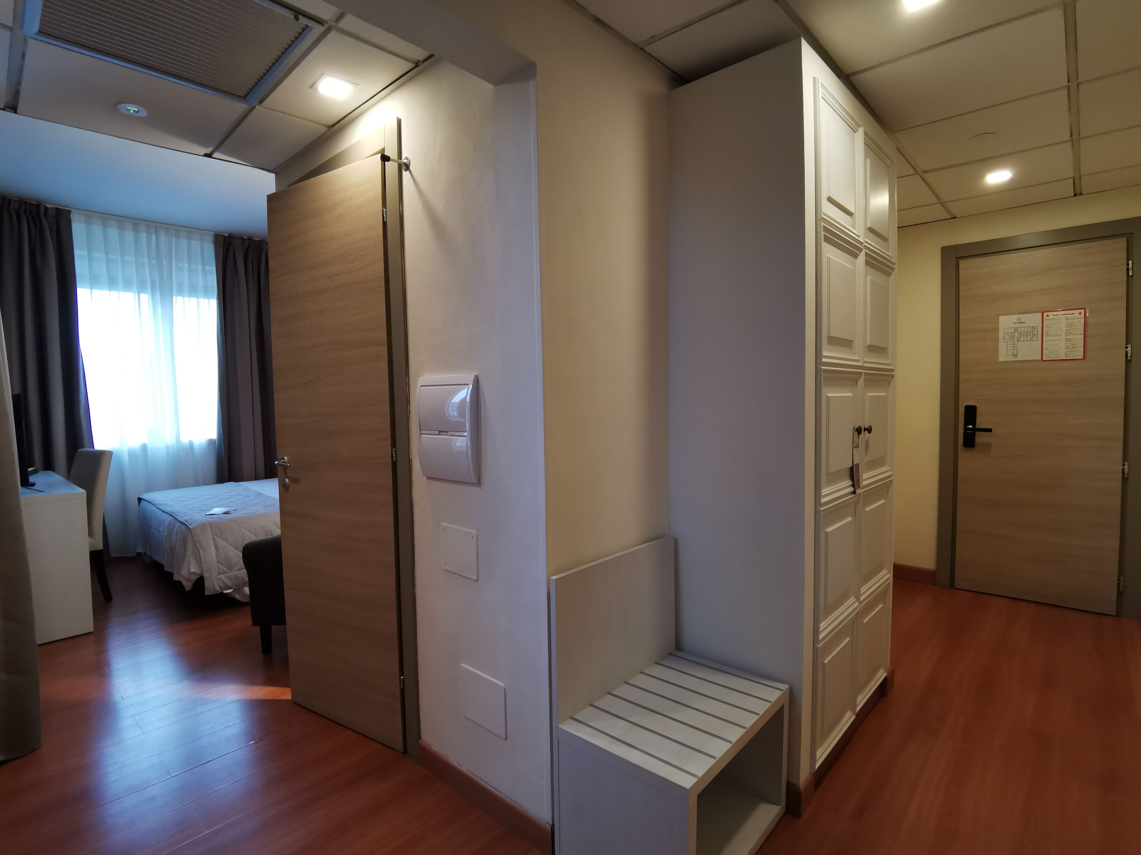 A hotel room with a bed, a desk, a wardrobe, and a shower area.