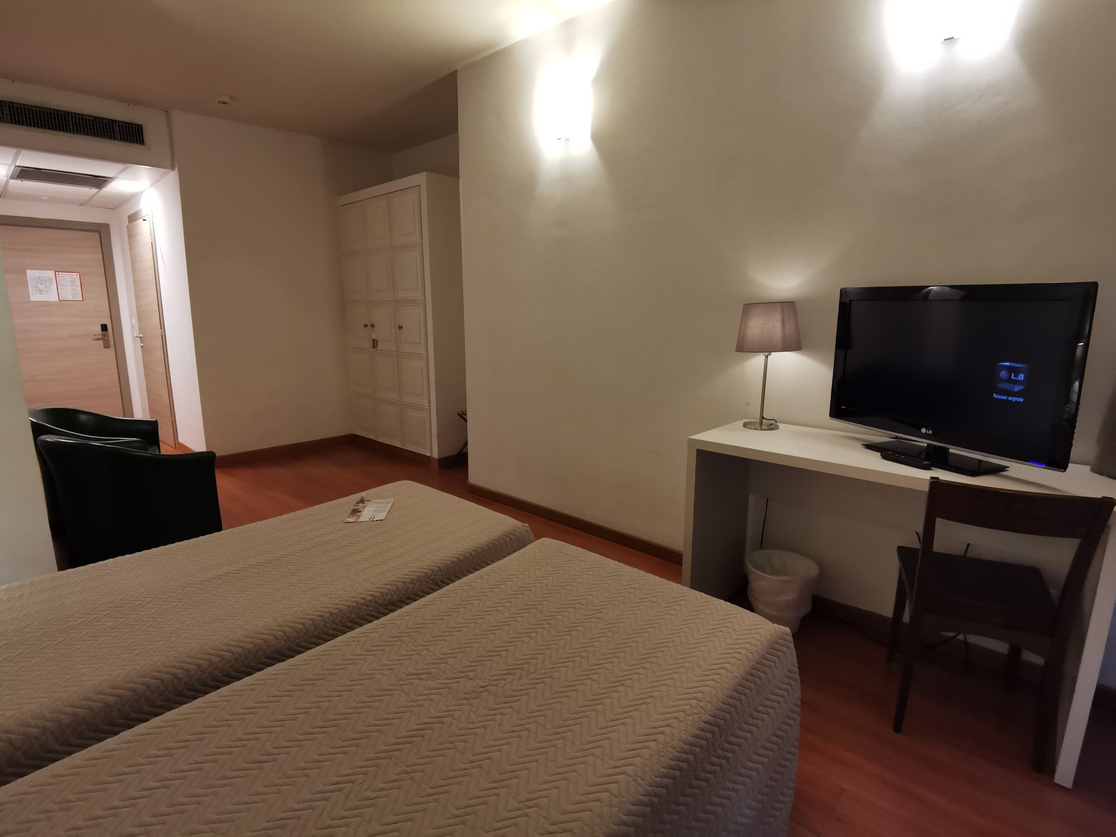 Habitación de hotel con dos camas, un escritorio con televisor, una lámpara y una silla.