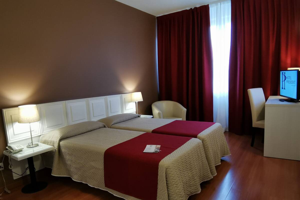 Habitación de hotel con dos camas, un escritorio, una silla, un televisor y un teléfono en la mesita de noche.