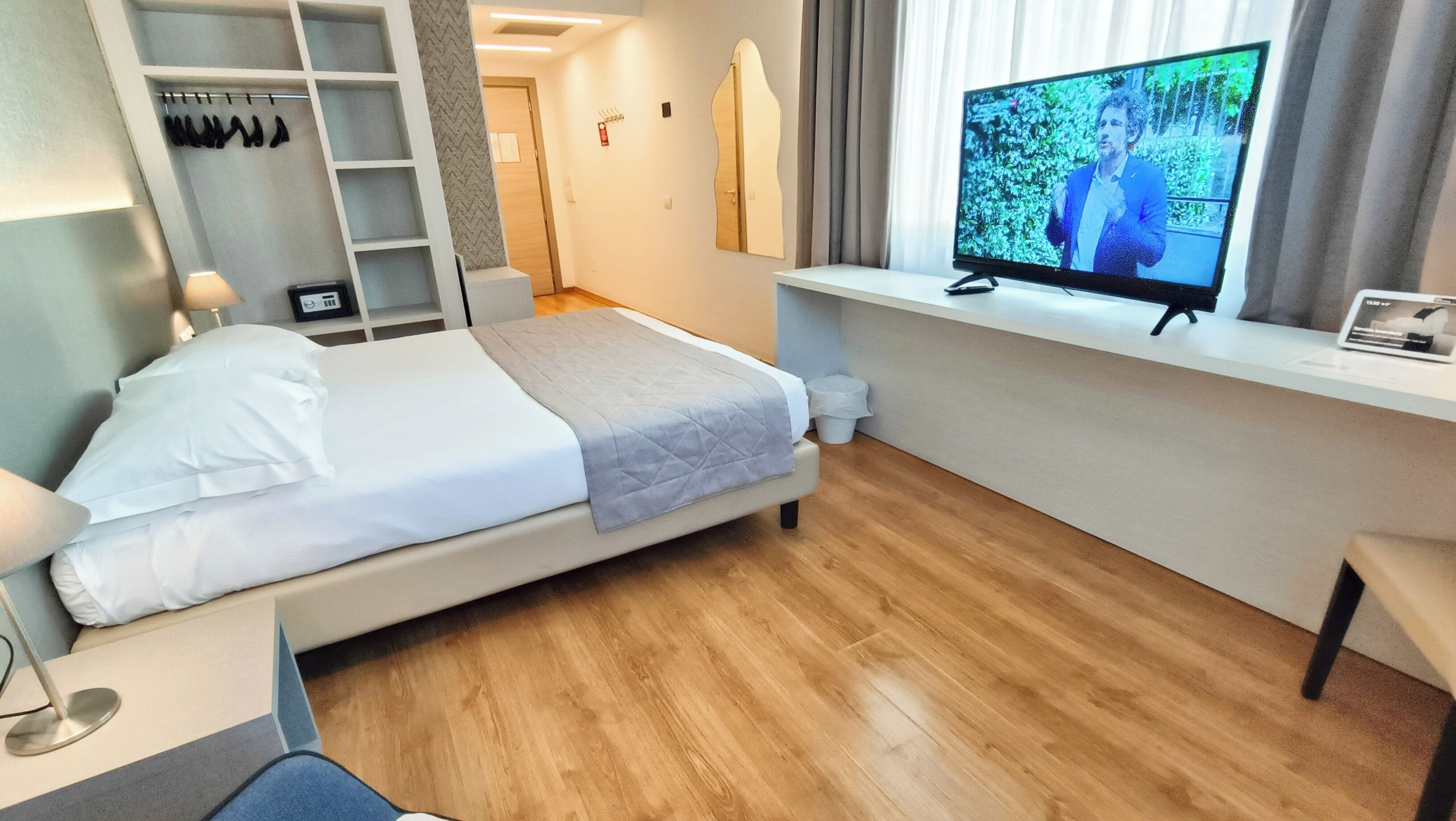 A hotel room with a bed, a desk, a television, a wardrobe, and a mirror.