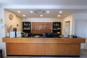 A hotel reception desk with a wooden counter, a clock on the wall, and a security camera.