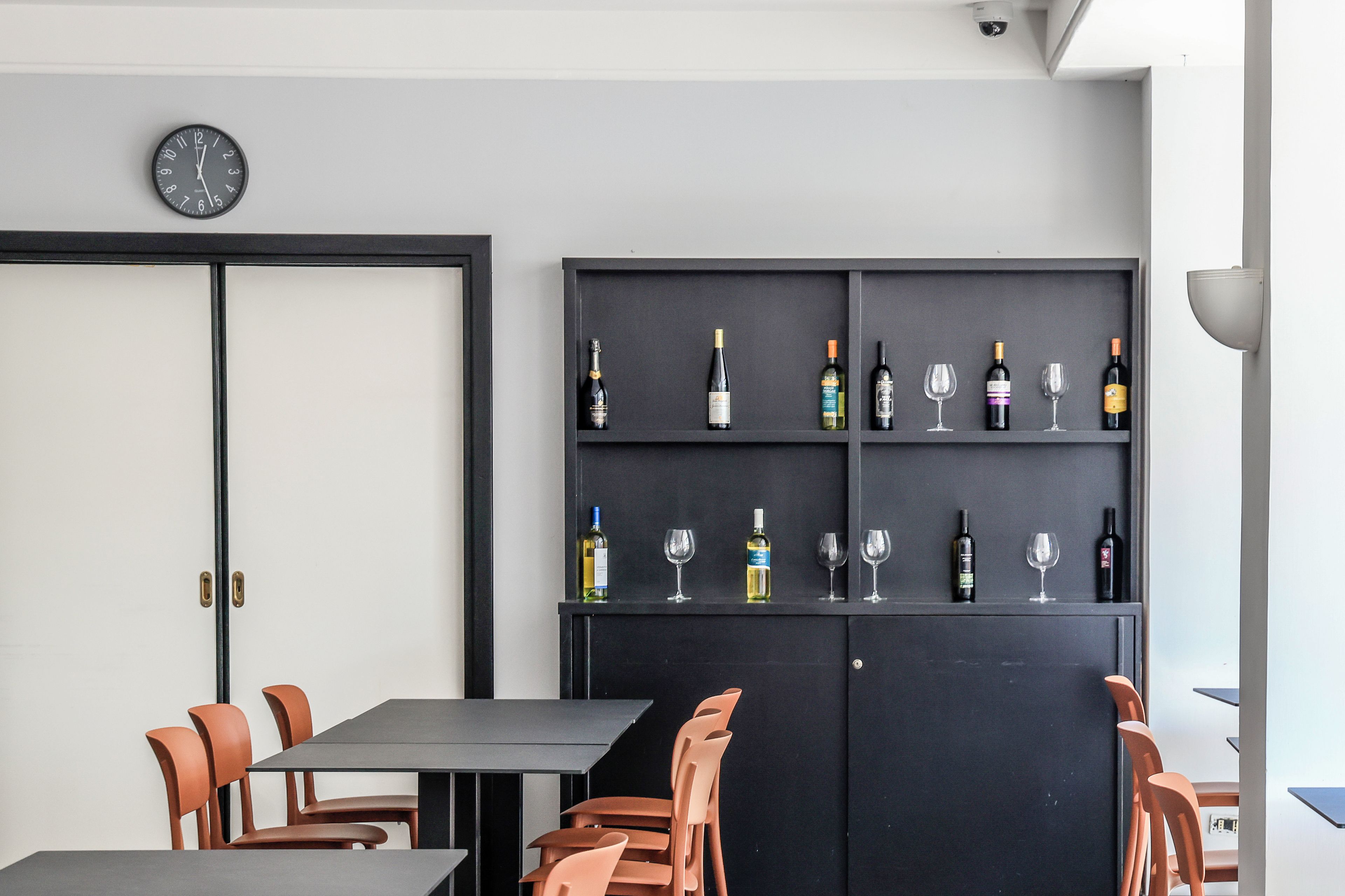 A dining area with a table and chairs, a wall-mounted clock, and a wine rack with bottles and glasses.