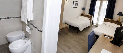 A hotel room with a bathroom, a bed, a desk, and a bedside table.