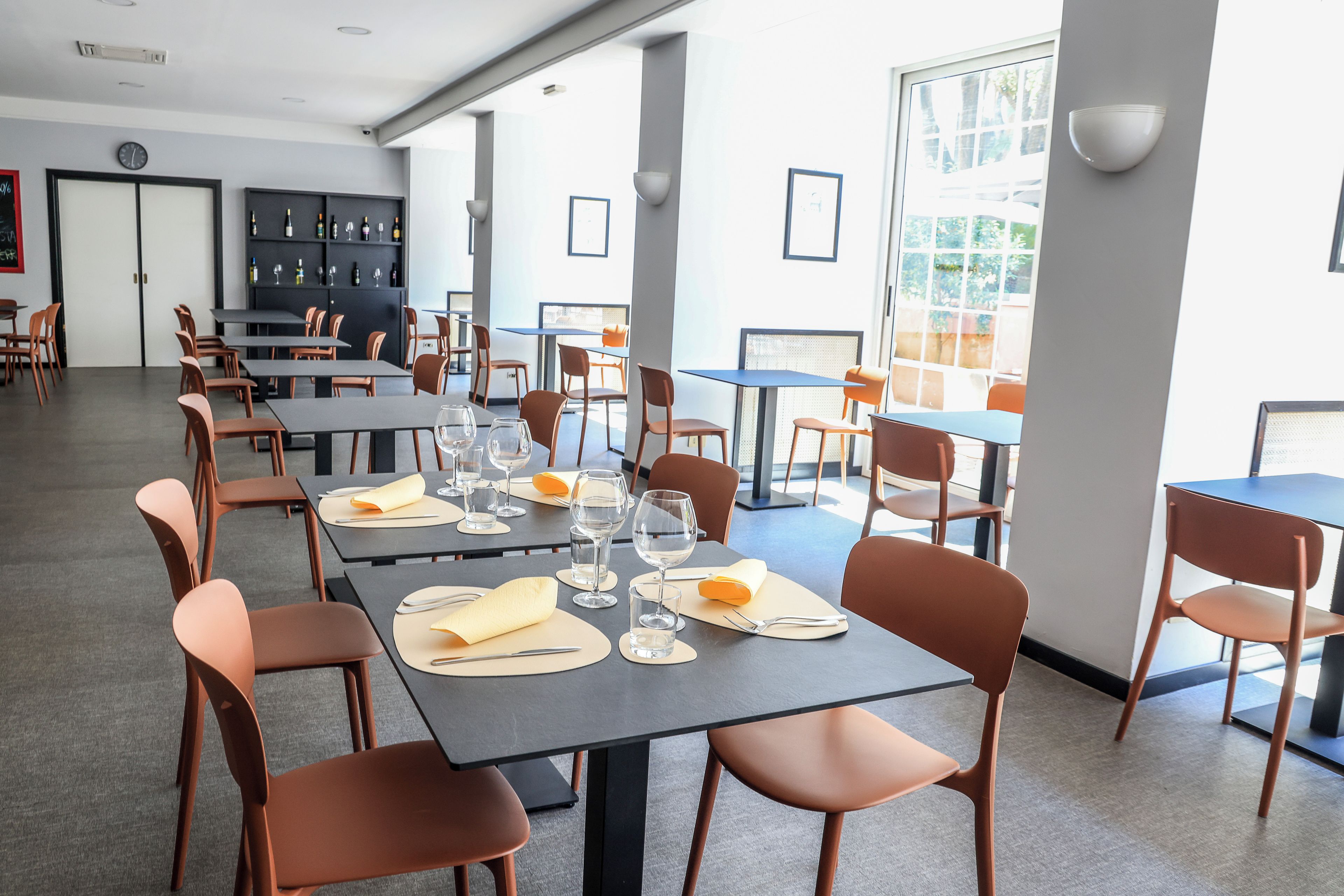 Een eetgedeelte met tafels voor twee personen, compleet met bestek en glazen, en een bar met flessen en glazen.