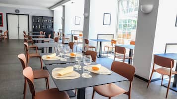 Een eetgedeelte met tafels voor twee personen, compleet met bestek en glazen, en een bar met flessen en glazen.