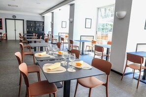 Un espace repas avec des tables préparées pour deux personnes, comprenant des couverts et des verres, ainsi qu’un bar avec des bouteilles et des verres.