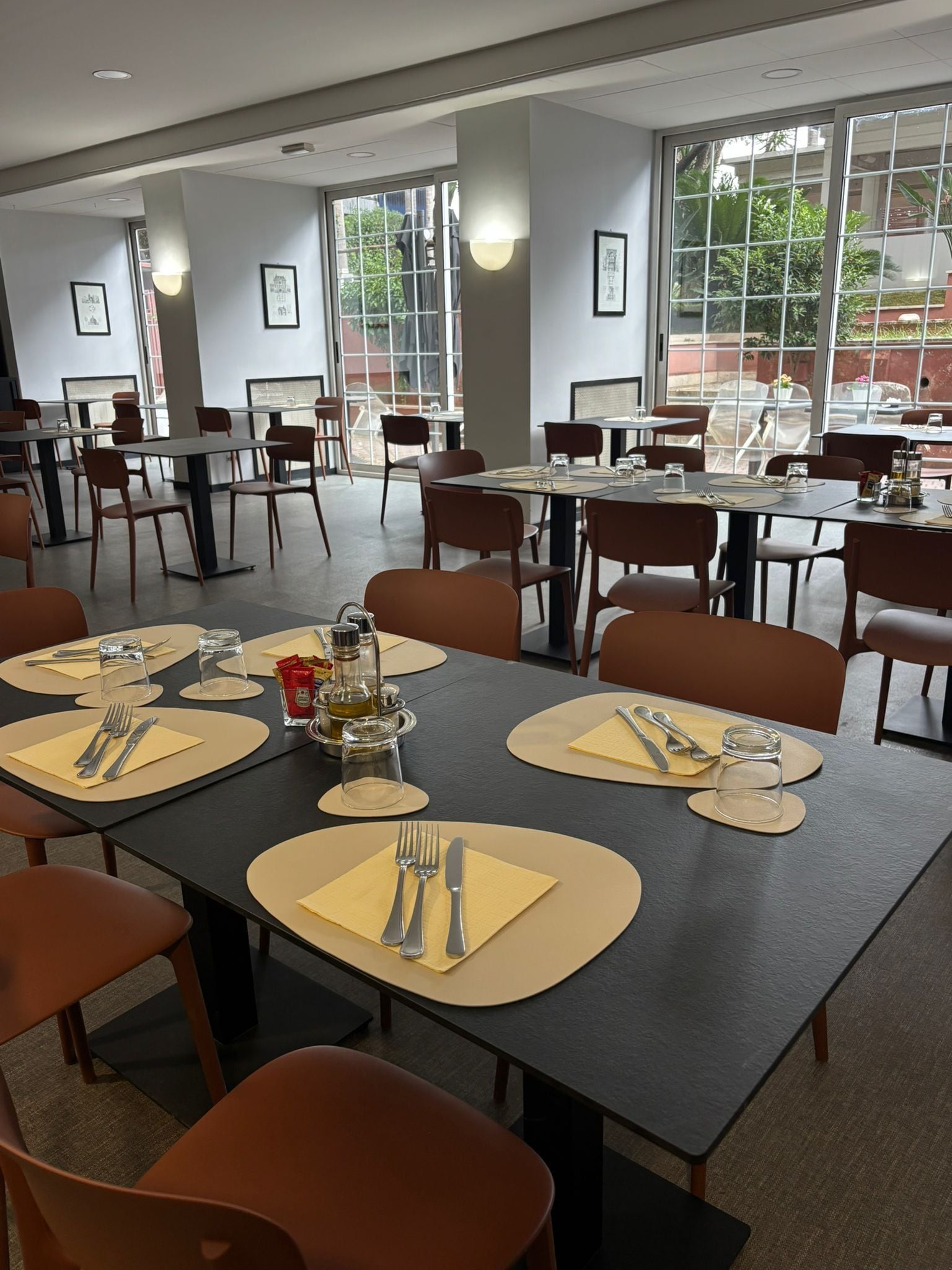 Un ristorante con diversi tavoli apparecchiati per la cena, caratterizzato da un design moderno, colori neutri e ampie finestre.