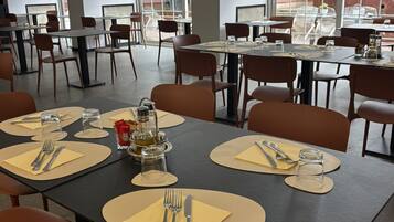 Un ristorante con diversi tavoli apparecchiati per la cena, caratterizzato da un design moderno, colori neutri e ampie finestre.