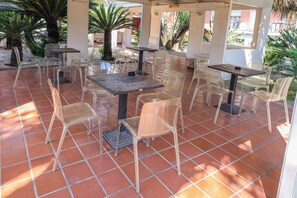 An outdoor patio with multiple tables and chairs, surrounded by a tiled floor and palm trees. - Hotel Giardino D'Europa (Rome)