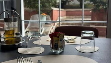 Une table dressée pour le repas, avec couverts, verres et condiments, donnant sur un jardin par une fenêtre.