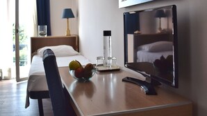 Een hotelkamer met een bed, een bureau met een schaal fruit, een lamp en een grote spiegel.