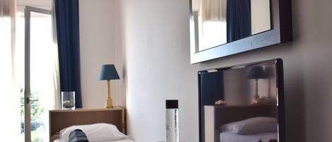 A hotel room with a bed, a desk with a bowl of fruit, a lamp, and a large mirror.