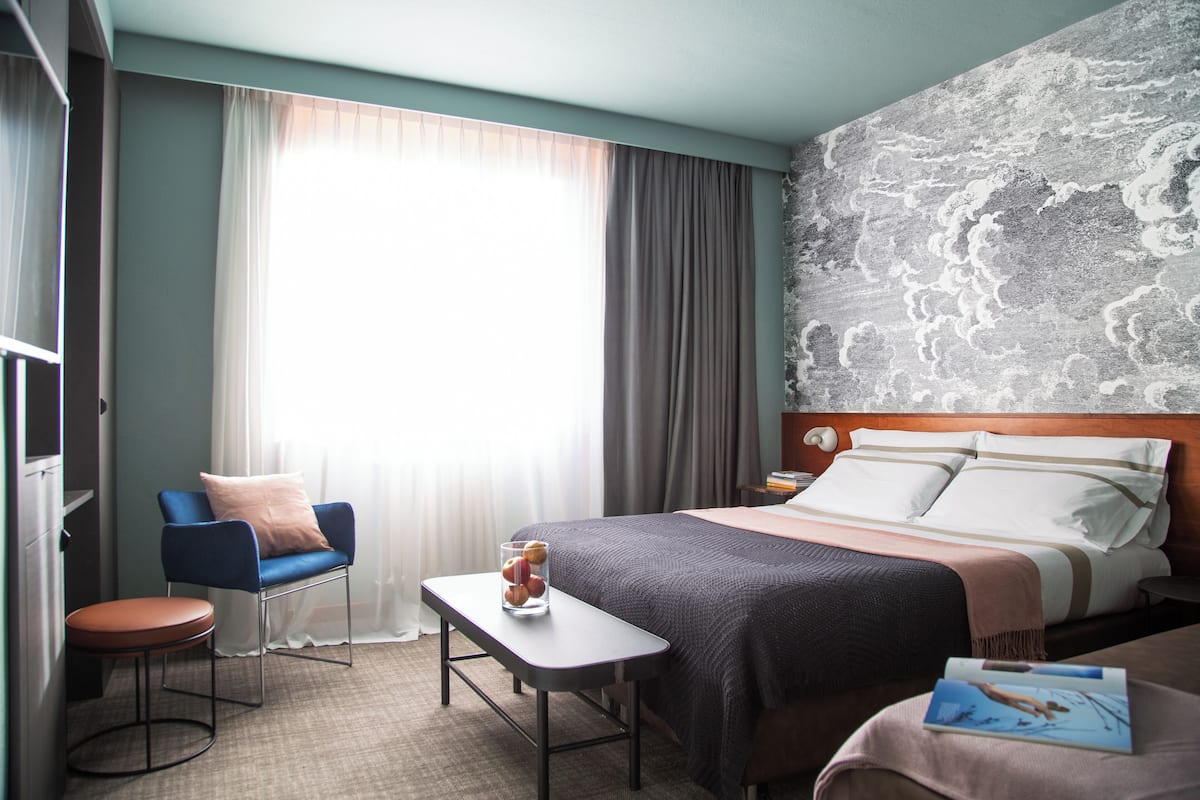 A hotel room with a bed, a desk, a chair, and a window with curtains.