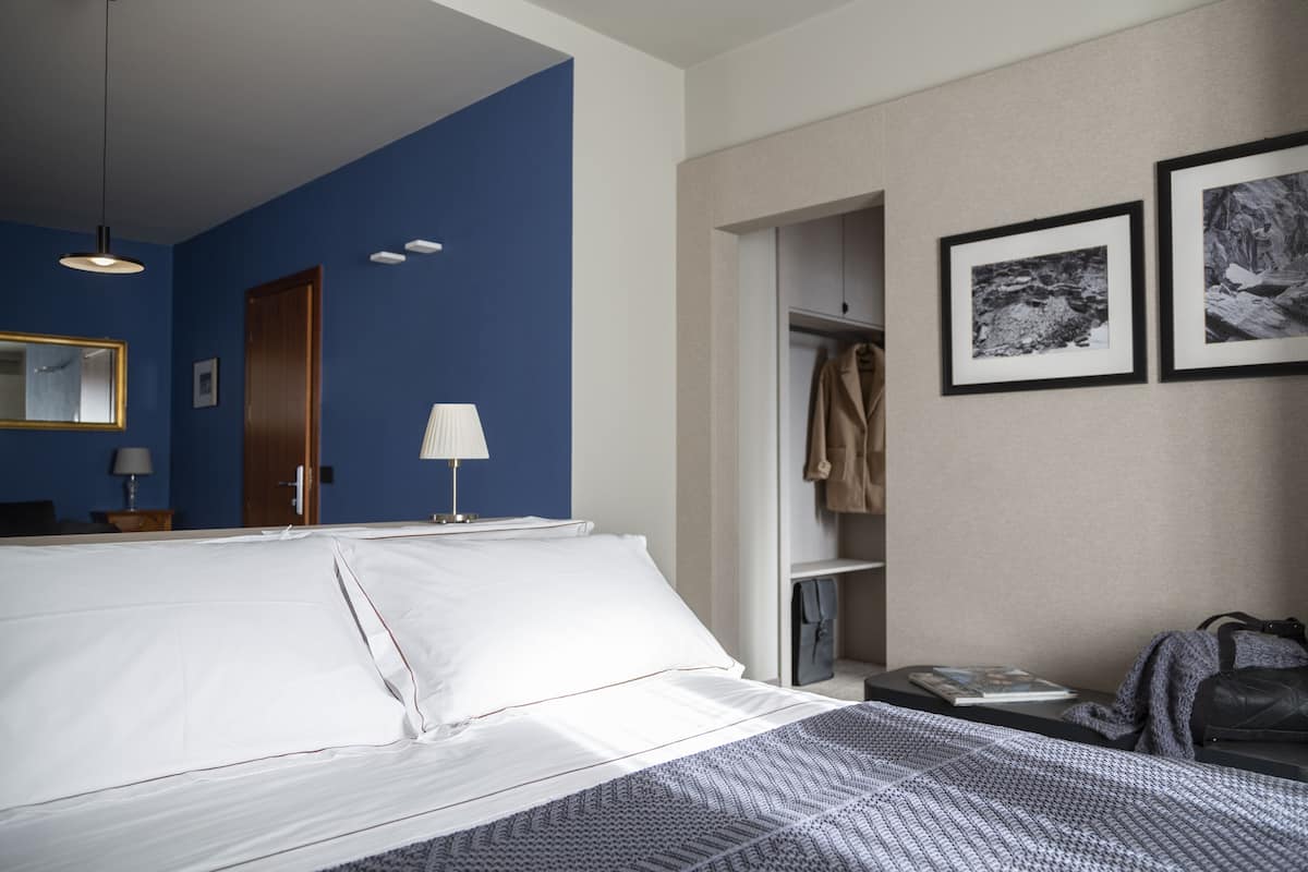 A hotel room with a bed, a wardrobe, a mirror, and two framed pictures on the wall.