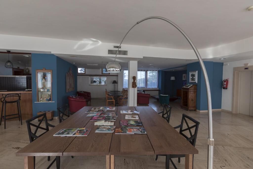 Uma ampla sala de jantar com uma longa mesa de madeira, rodeada por cadeiras, e uma moderna luminária pendente.