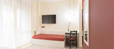 A hotel room with a bed, a desk, a chair, a TV, and a window with curtains.
