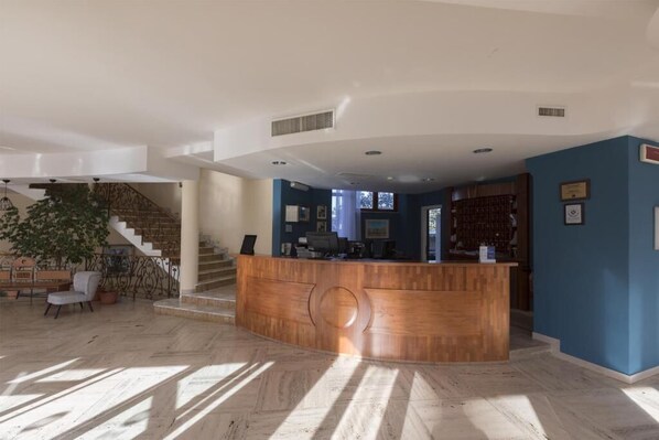 A spacious lobby with a wooden reception desk, a staircase, and a large potted plant.