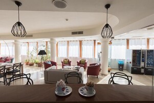 A spacious living area with a dining table set for two, surrounded by comfortable seating and large windows.