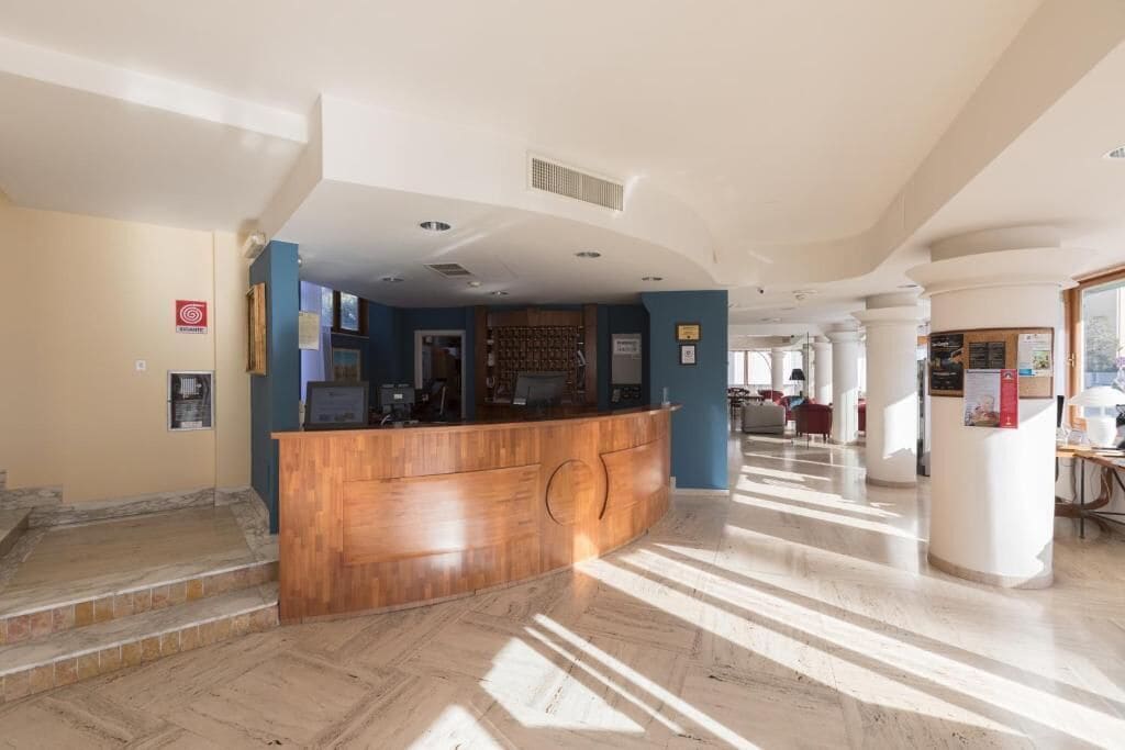 Eine Hotlellobby mit einer Rezeption, einer Treppe und Blick ins Freie.