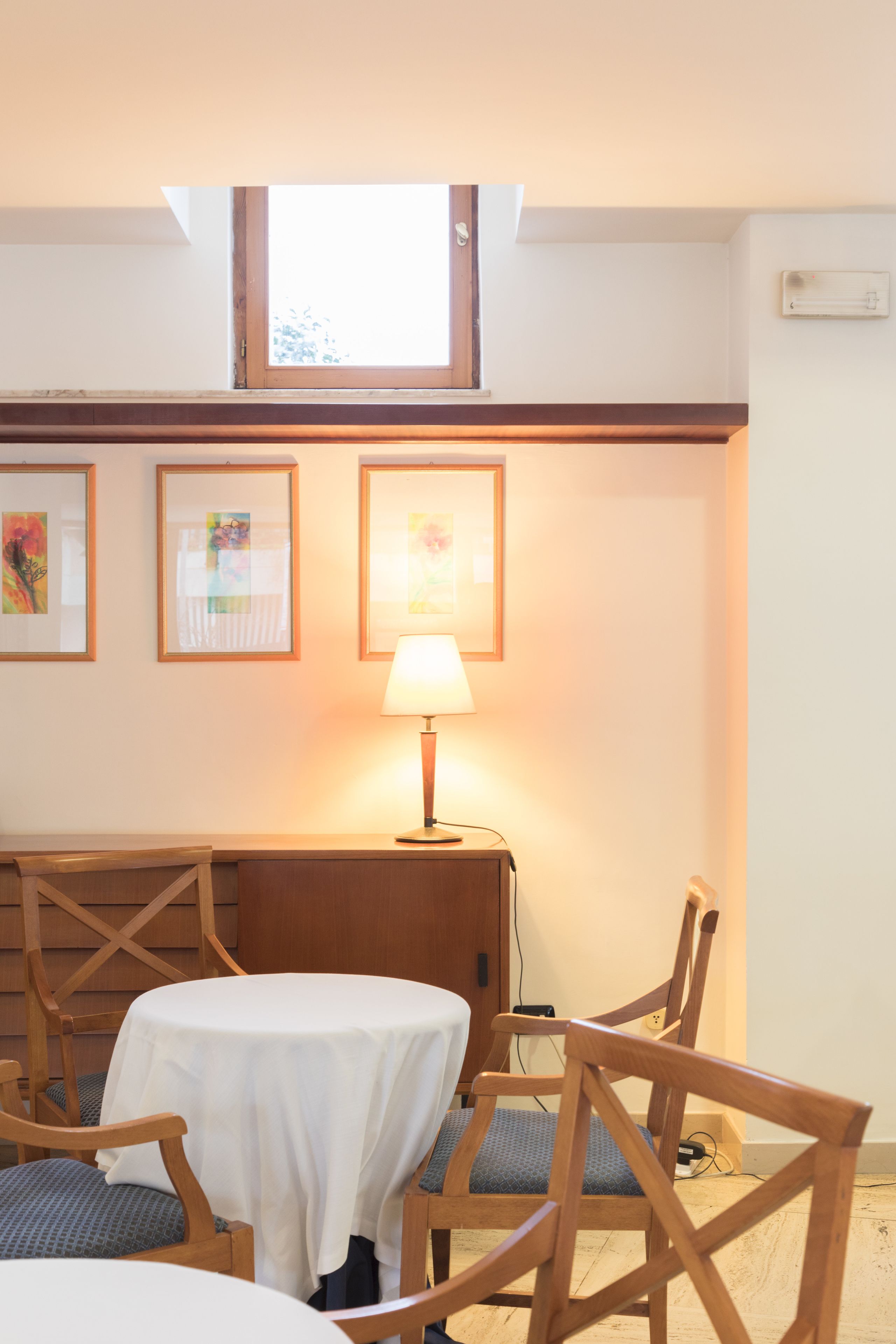 A room with a table, chairs, a lamp, and framed artwork on the wall.