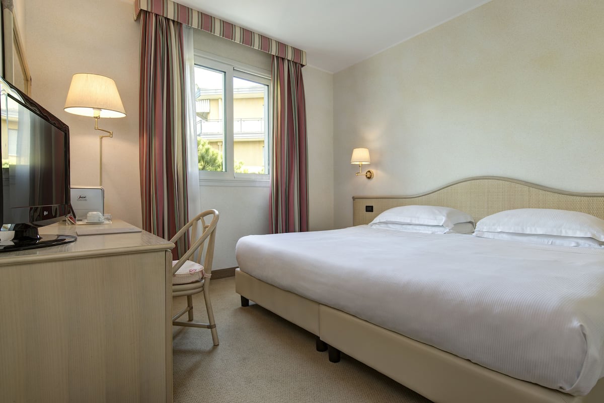 Een hotelkamer met een bed, een bureau met een computer, een stoel en twee bedlampjes.