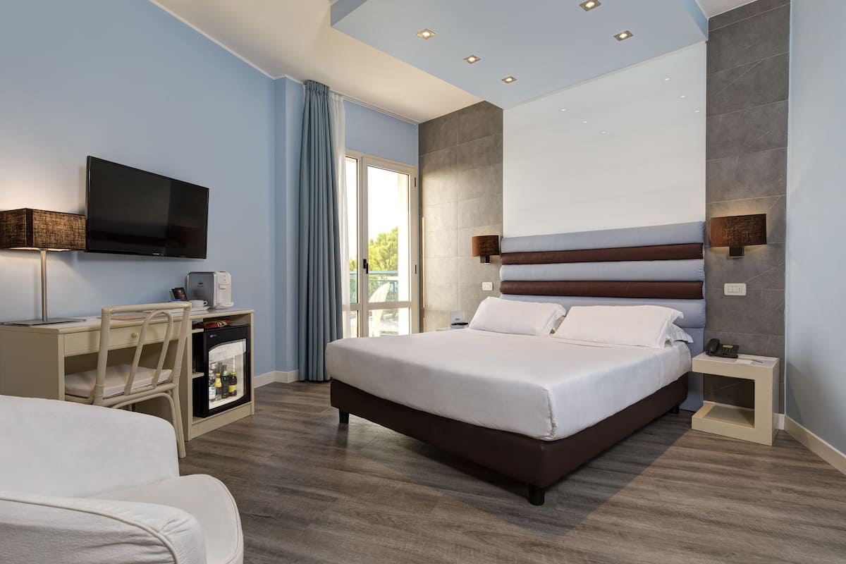 Een moderne hotelkamer met een groot bed, een bureau met een computer, een televisie en een minibar.