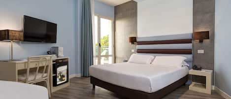 A modern hotel room with a large bed, a desk with a computer, a television, and a minibar.