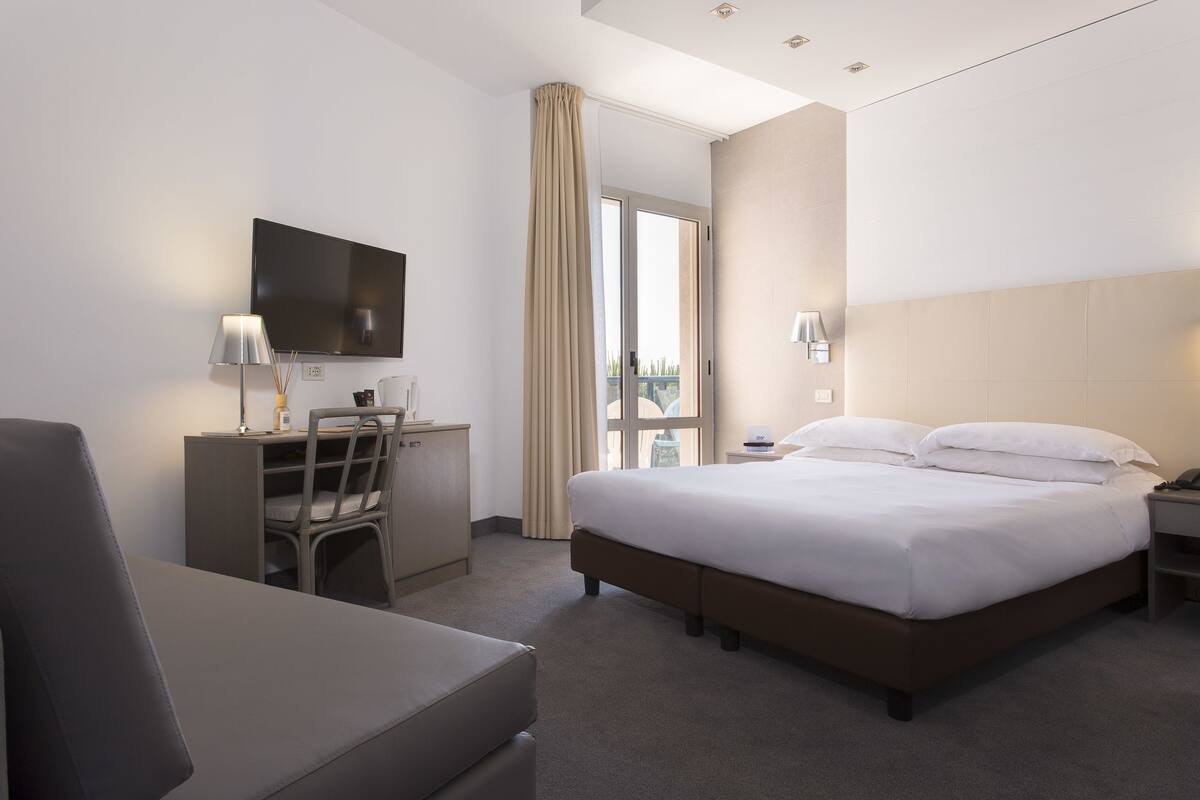 Een hotelkamer met een bed, bureau, stoel en een televisie aan de muur.